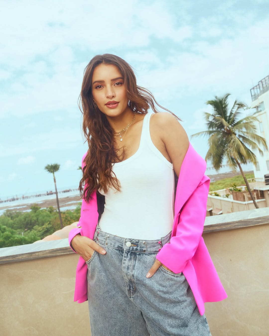Tripti Dimri posing outdoors in a pink blazer, denim jeans, and sunglasses against a sunny backdrop.