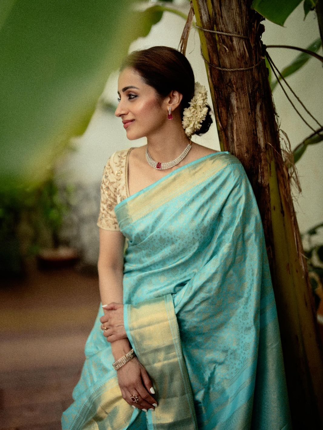 Trisha Krishnan draped in a vibrant blue saree with gold detailing, adorned with floral accessories.