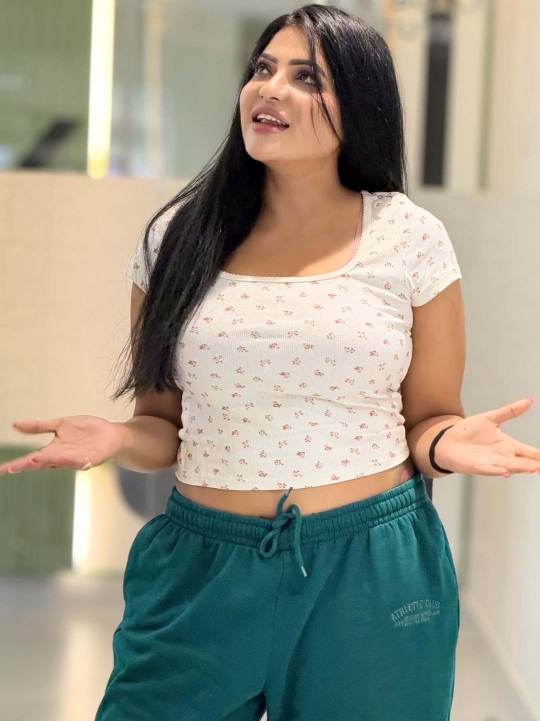 Reshma Pasupuleti stands indoors, wearing a white cropped top and deep teal joggers.