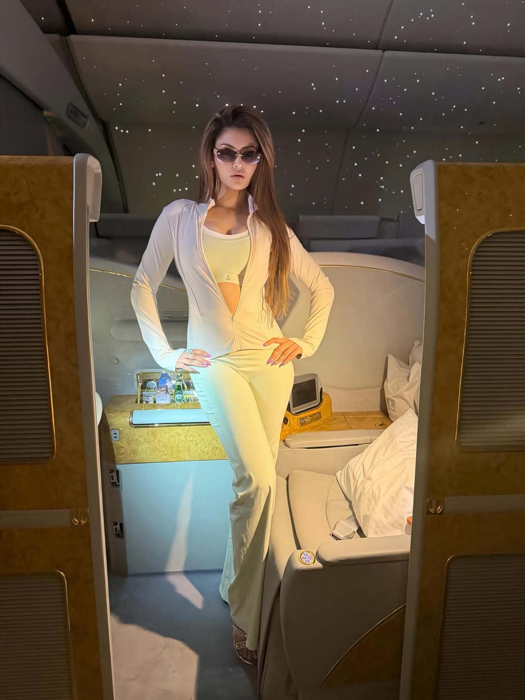 Urvashi Rautela poses in a monochromatic cream two-piece set inside a luxury coach setting.