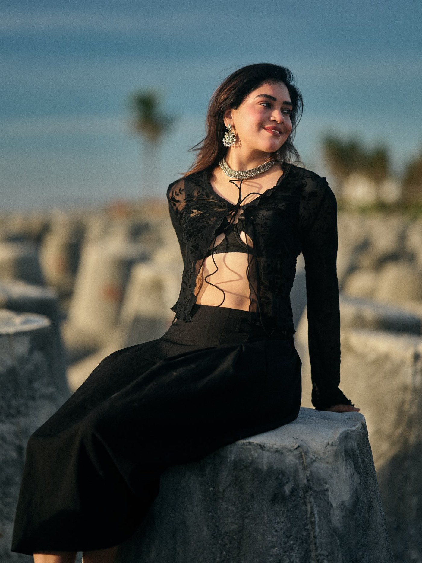 Varshini Venkat poses elegantly against a scenic waterfront backdrop showcasing stunning black ensembles.